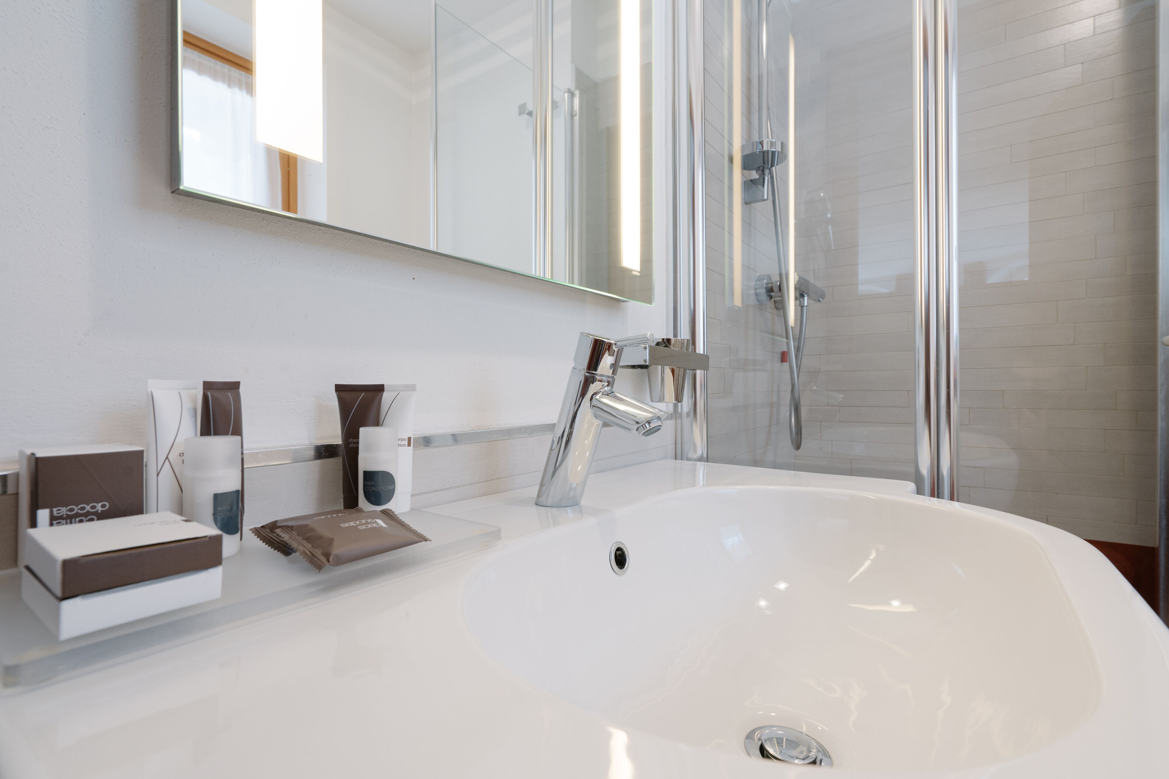 A modern bathroom with a large white sink, a glass shower enclosure, and a mirror above the sink.
