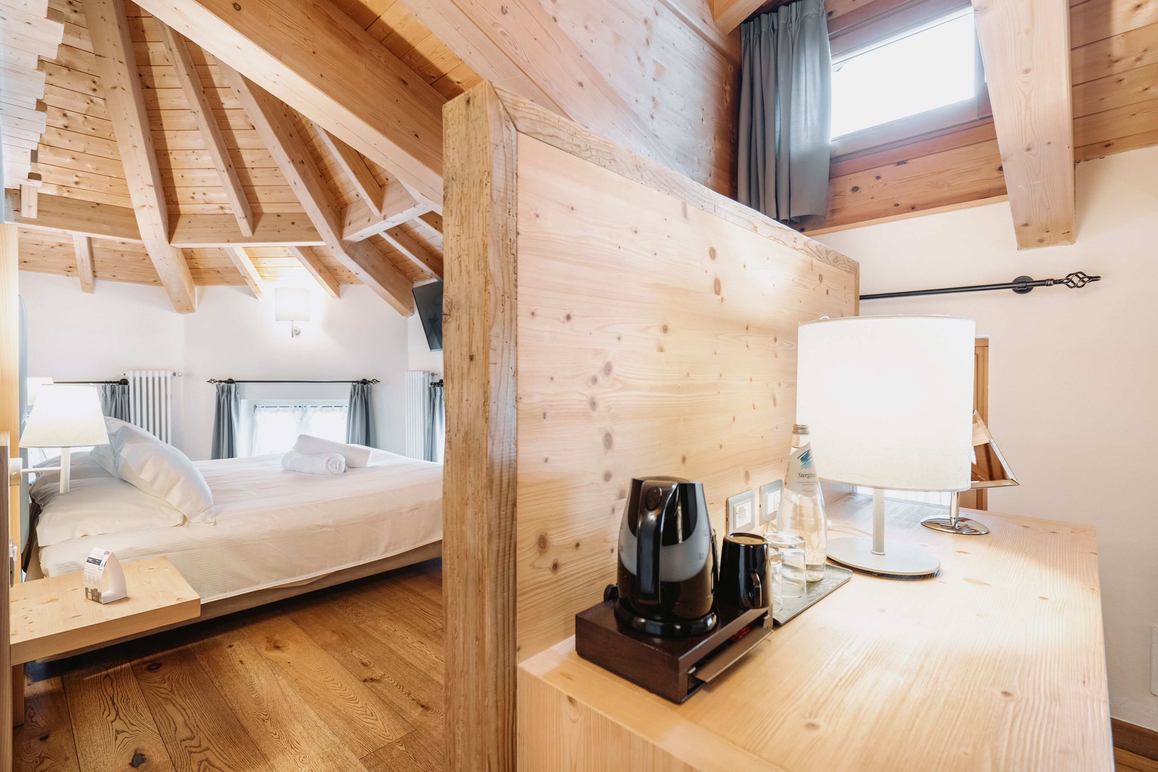 A wooden-framed room with a bed, a desk with a lamp, and a coffee maker.