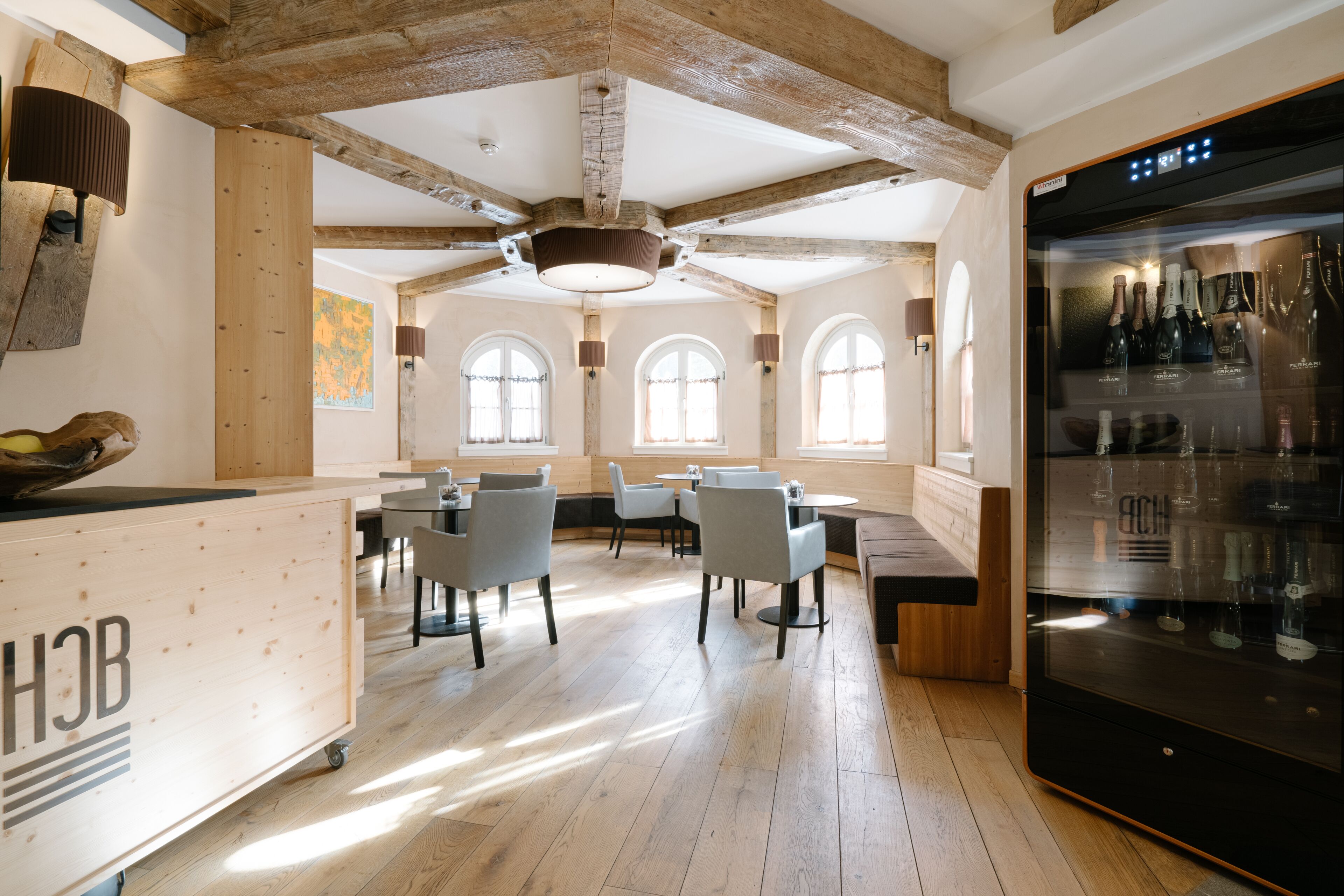 A spacious dining area with wooden beams, large windows, and a modern refrigerator stocked with wine.