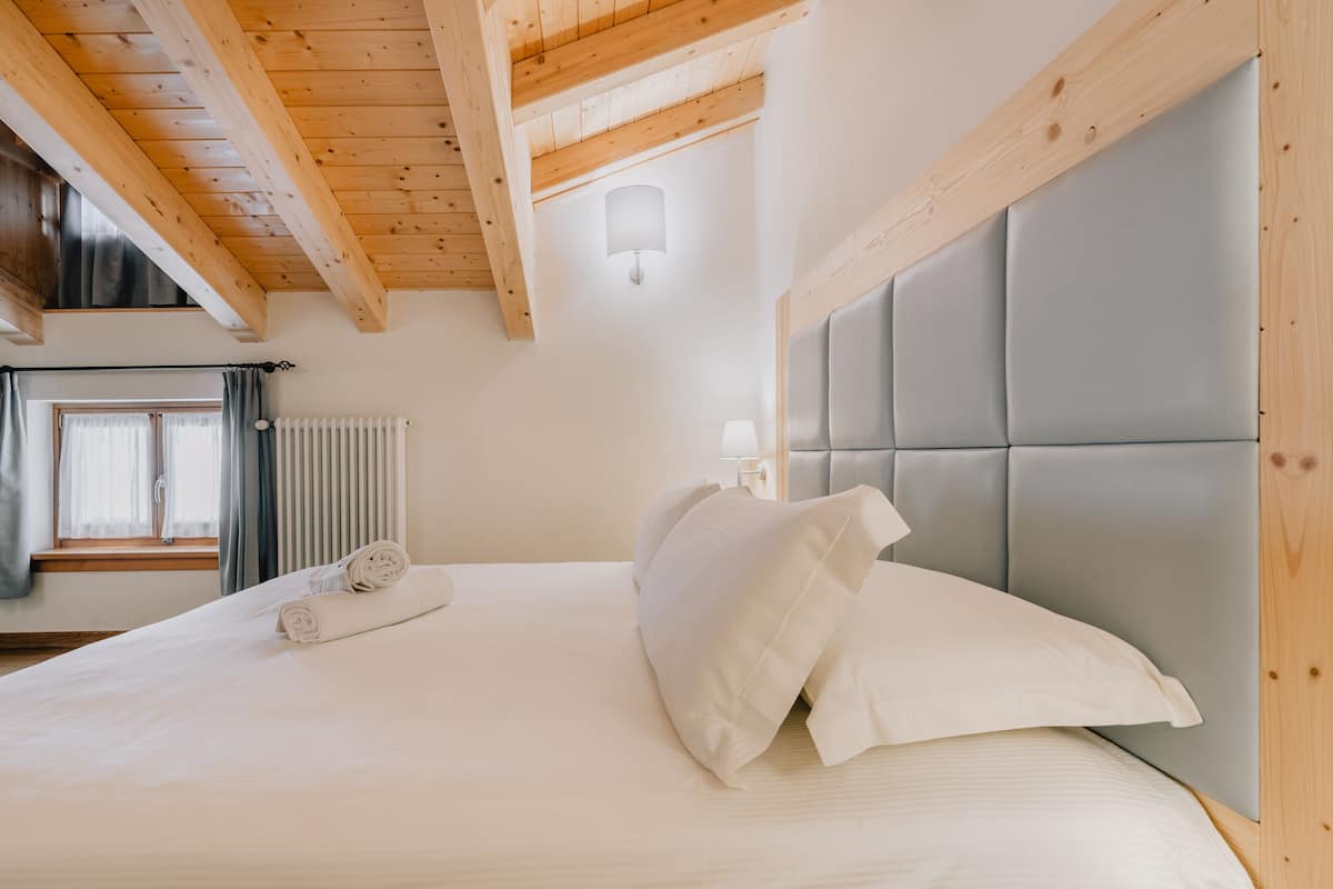 A bedroom with a wooden ceiling, a bed with white bedding, and a window with curtains.