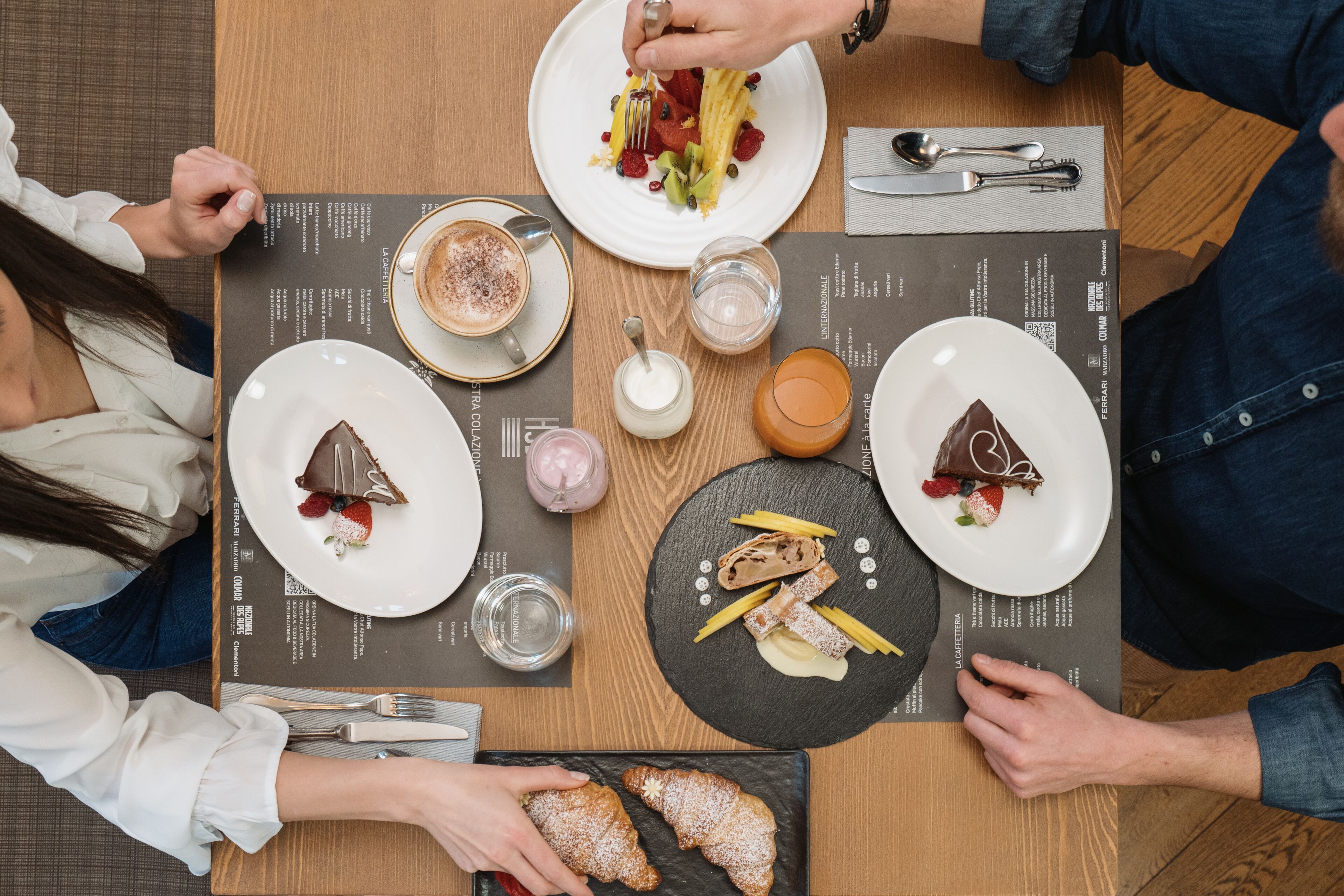 A table set with various dishes, including a plate with a chocolate dessert, a plate with a croissant, and a plate with a salad.