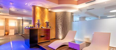 A modern spa area with wooden flooring, two white cushioned chairs, a wooden cabinet with a decorative item, and a textured wall.