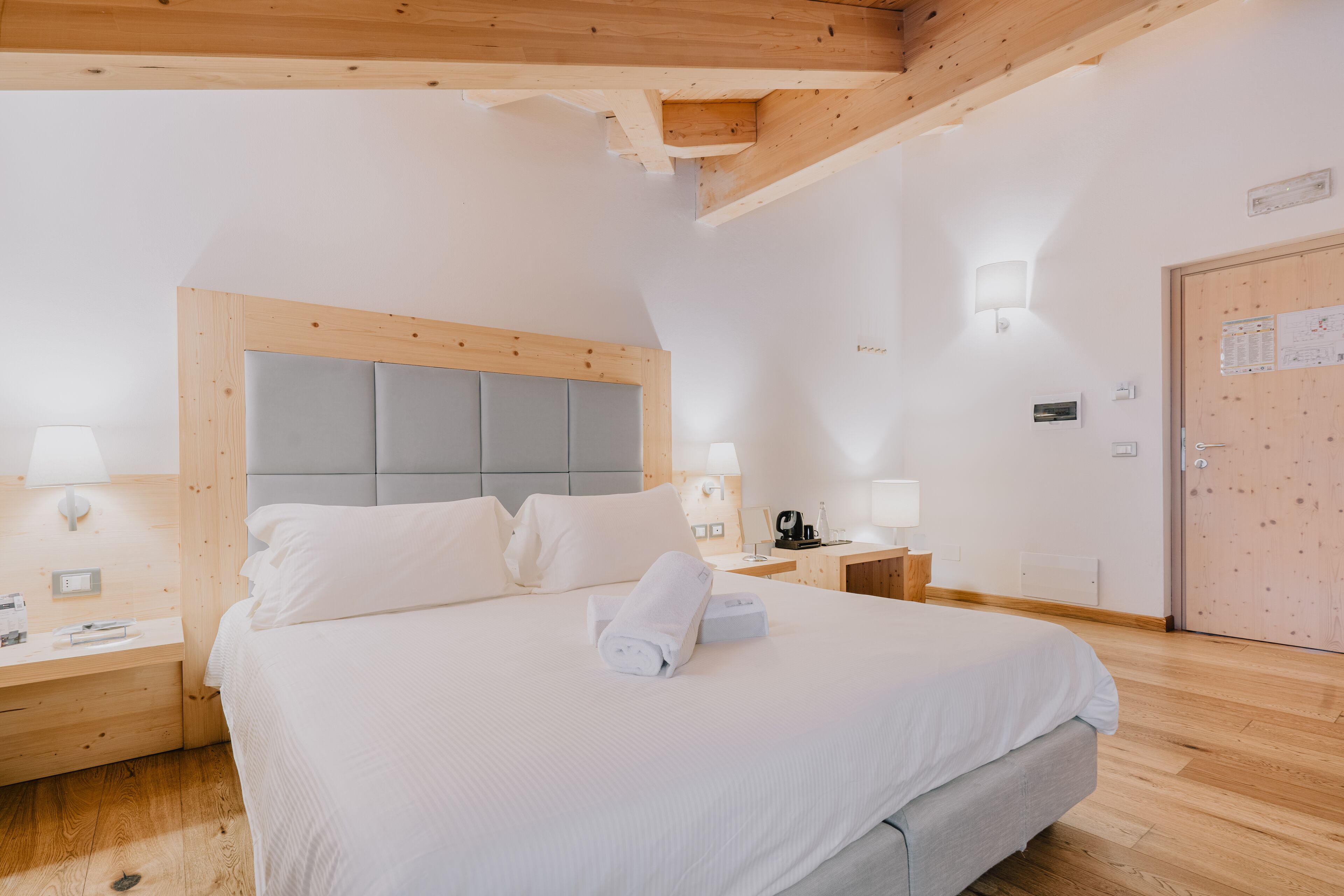 A bedroom with a large bed, wooden headboard, bedside tables with lamps, and a wooden door with a bulletin board.