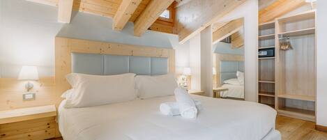 A bedroom with a large bed, wooden ceiling beams, a walk-in closet, and a nightstand with a lamp.