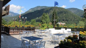 An outdoor patio with tables and chairs, a flag, and a mountainous backdrop.