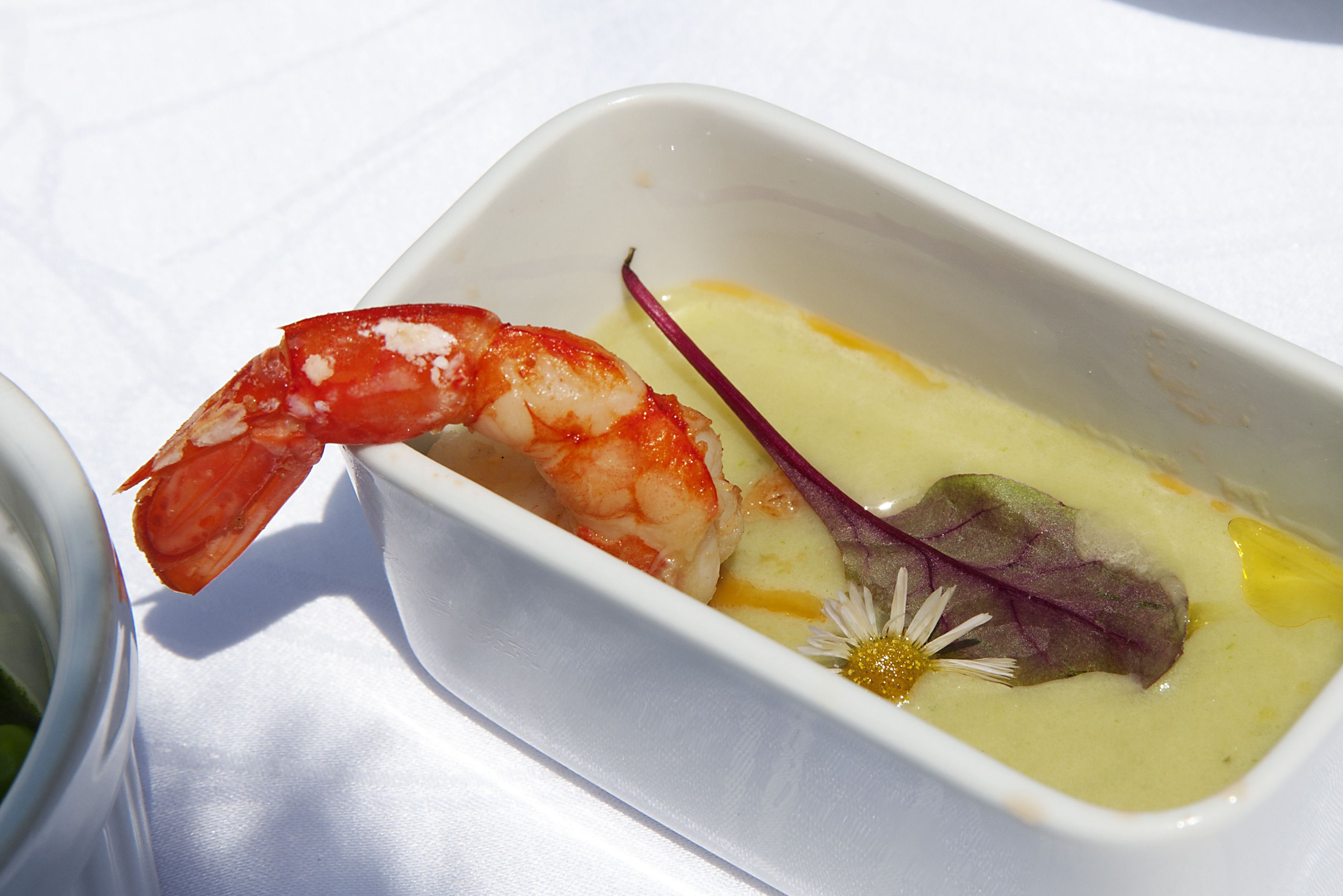 A dish with a shrimp and a flower in a white bowl.
