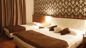 A hotel room with two beds, wooden flooring, a patterned wall, and a nightstand with a lamp.