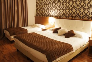 Quarto de hotel com duas camas, piso de madeira, parede estampada e mesa de cabeceira com abajur.
