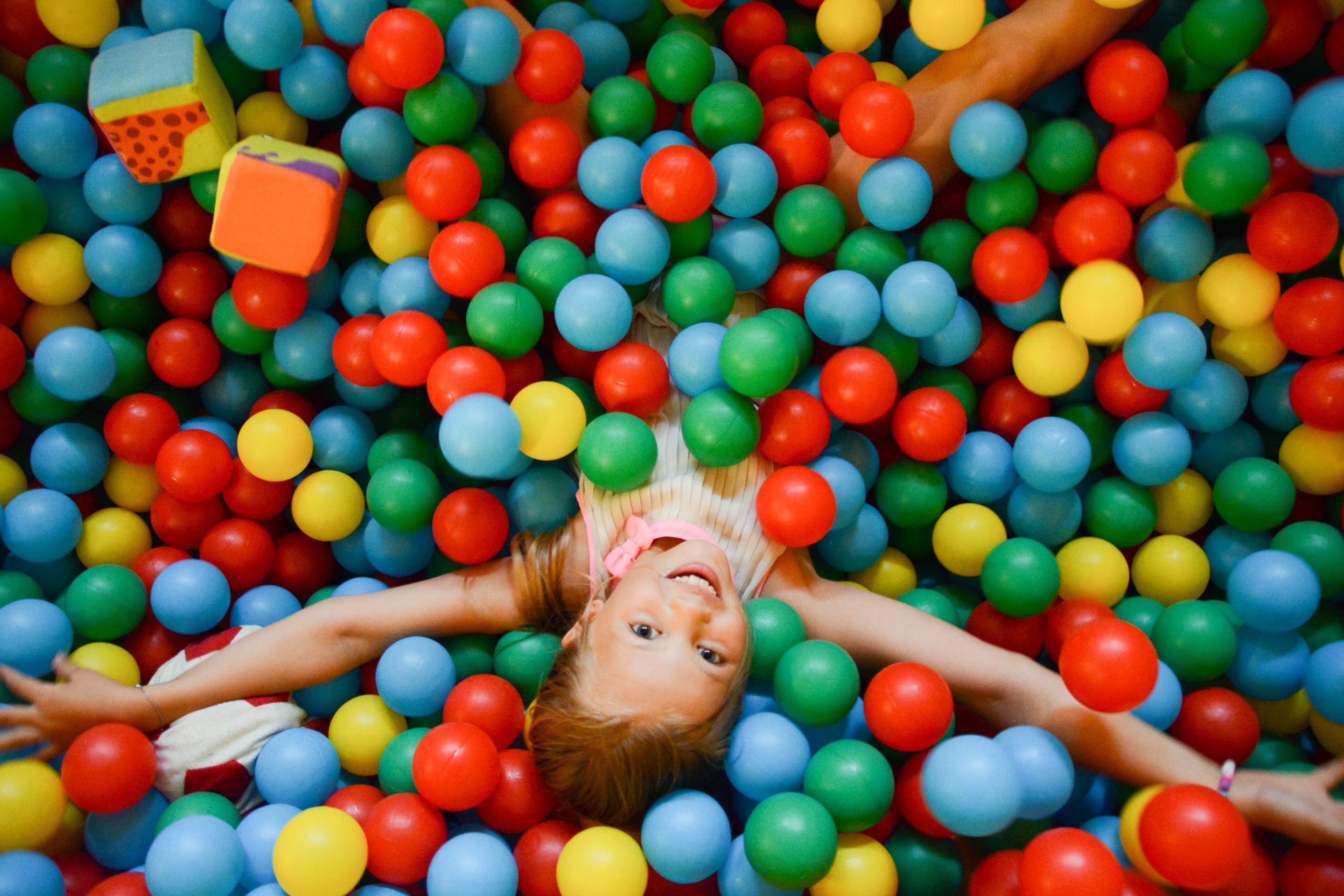 A child lying in a ball pit filled with multicolored balls.