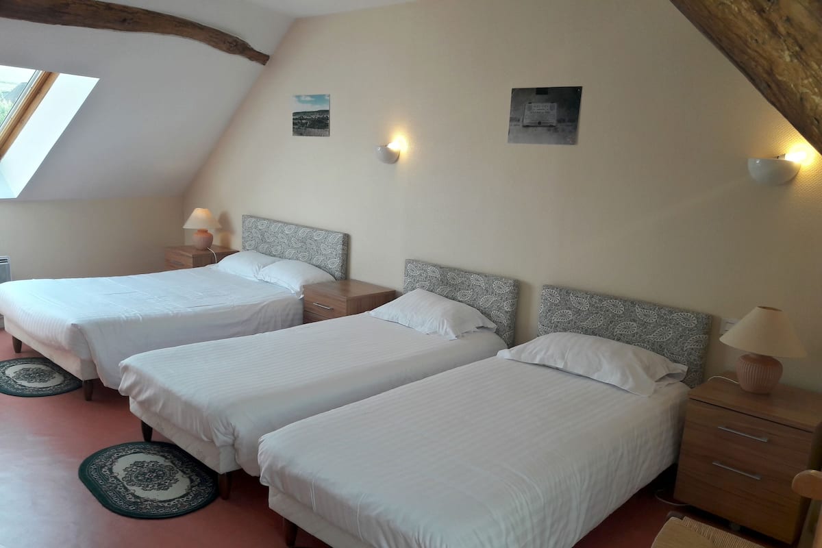 Ein Zimmer mit drei Betten, einer Holzbalkendecke und einem kleinen Fenster.