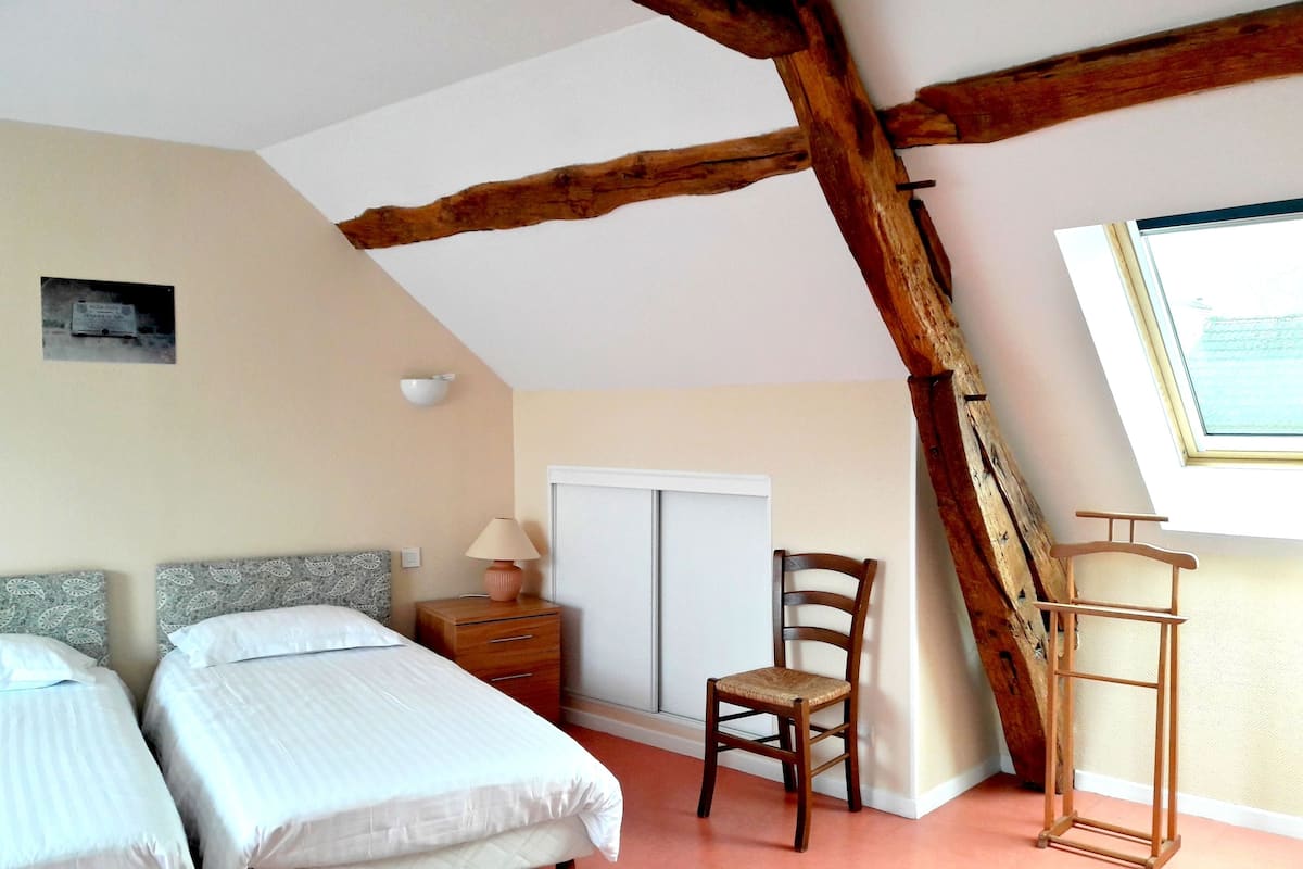 Ein Schlafzimmer mit zwei Betten, einem hölzernen Stuhl, einem Nachttisch mit Lampe, einem Kleiderschrank und einem Fenster mit Blick.