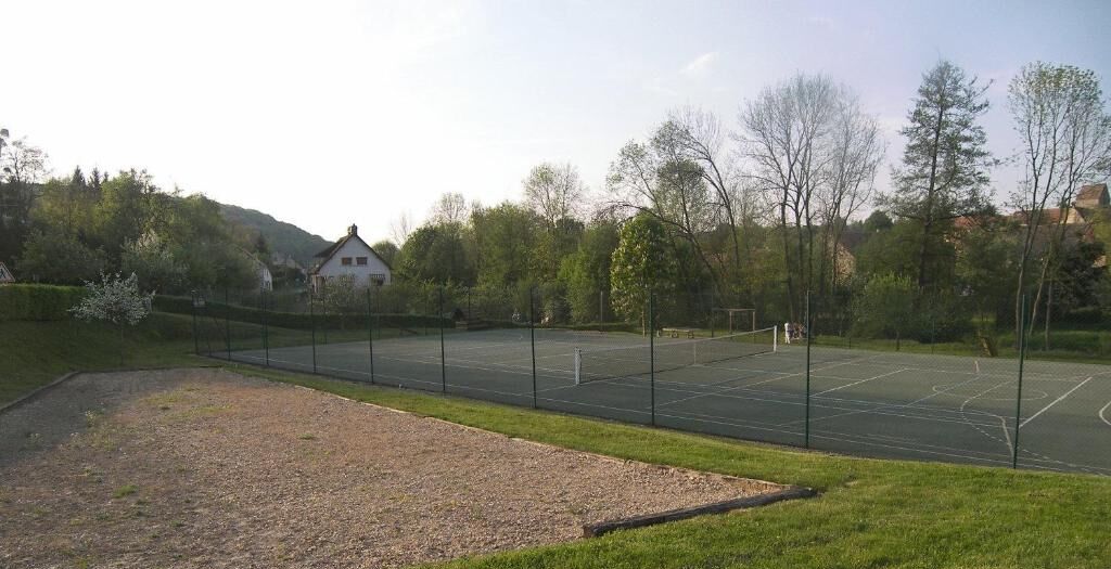 An outdoor tennis court surrounded by trees and a building in the background.