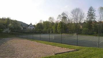 An outdoor tennis court surrounded by trees and a building in the background.