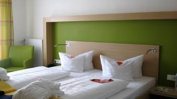 Habitación de hotel con cama, dos almohadas decoradas con corazones, una silla verde y una toalla sobre la cama.