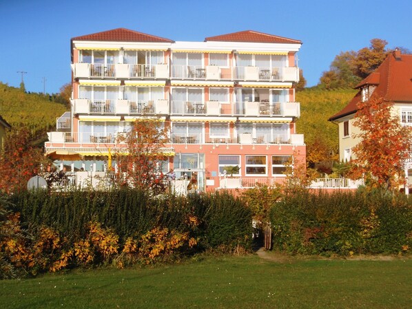 A multi-story hotel with balconies, a garden area in front, and a hilly backdrop. - Seehotel Off (Meersburg)