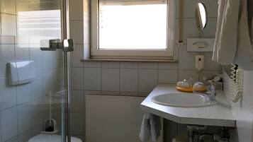 Un baño con cabina de ducha de vidrio, inodoro, lavamanos con espejo y ventana que proporciona luz natural.