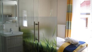 Ein modernes Badezimmer mit Duschkabine aus Glas, einem Waschbecken und einem Bett mit Handtuch.