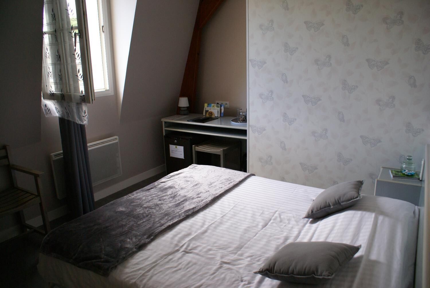 A bedroom with a bed, pillows, a desk, and a window with curtains.