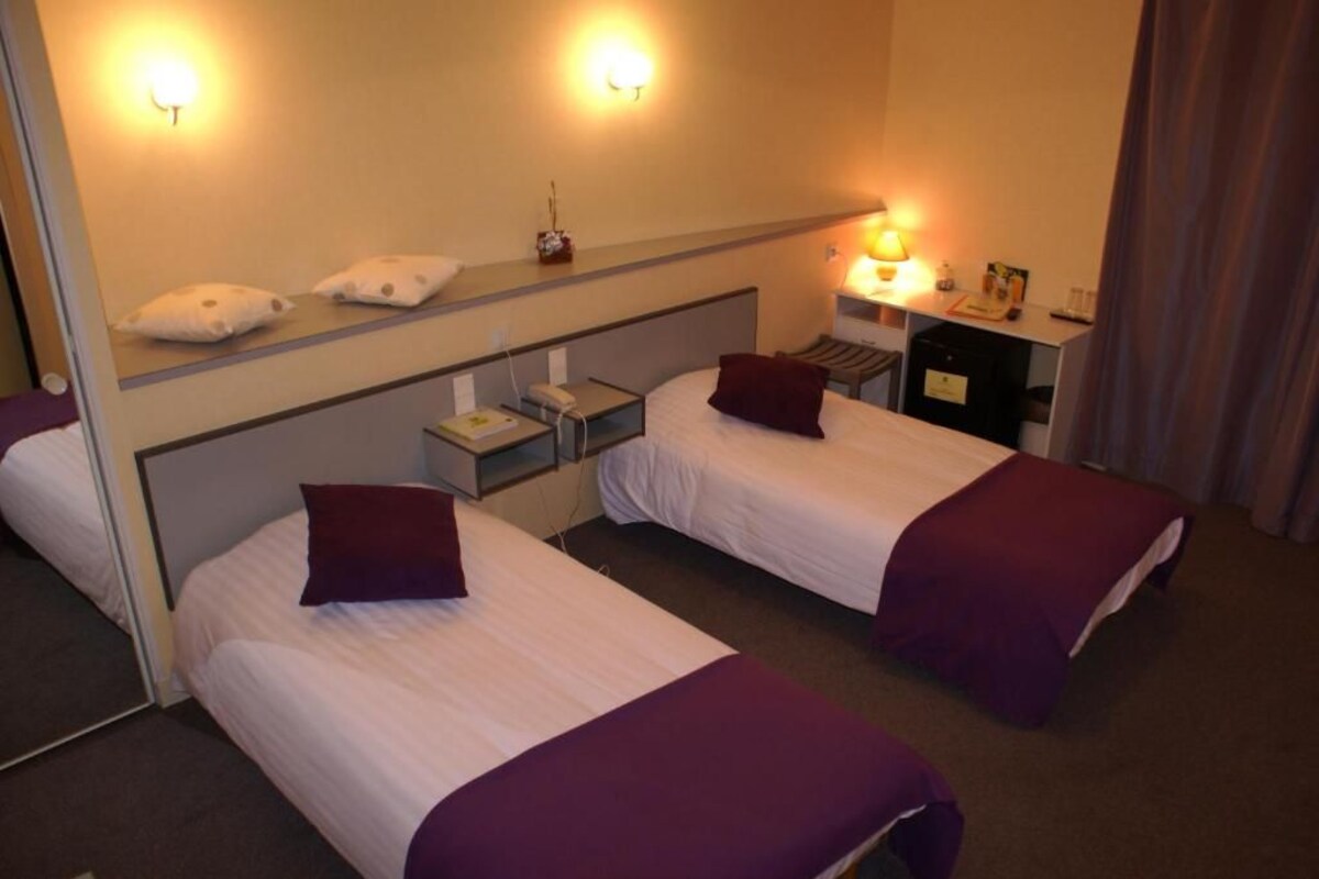 Une chambre d’hôtel avec deux lits, une table de chevet avec une lampe, un miroir et un bureau avec une chaise.