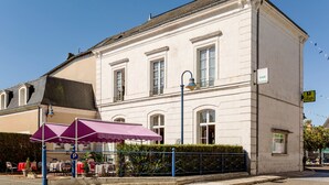 A white building with a balcony and a cafe with a purple awning.