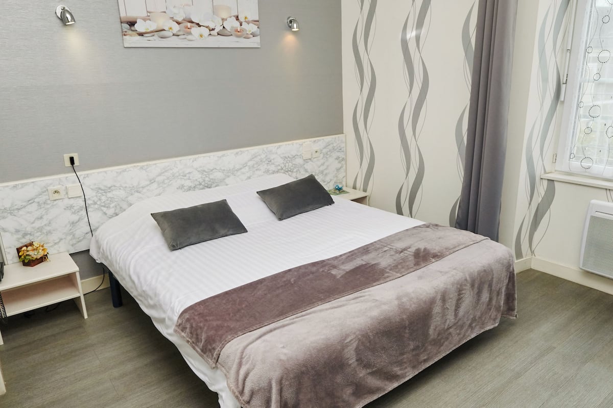 A neatly made bed with a white and brown blanket, a marble headboard, and a small bedside table with a lamp and a flower arrangement.