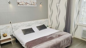 A neatly made bed with a white and brown blanket, a marble headboard, and a small bedside table with a lamp and a flower arrangement.