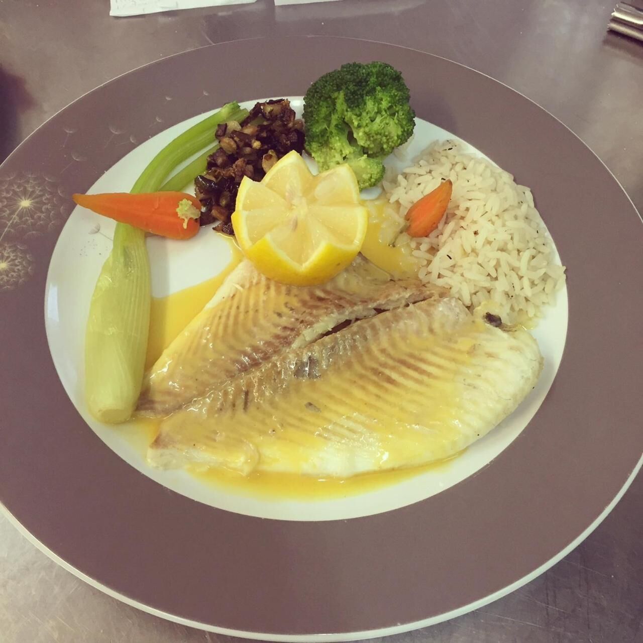 En tallerken med fisk, ris, broccoli, gulerødder og skiver af citron.