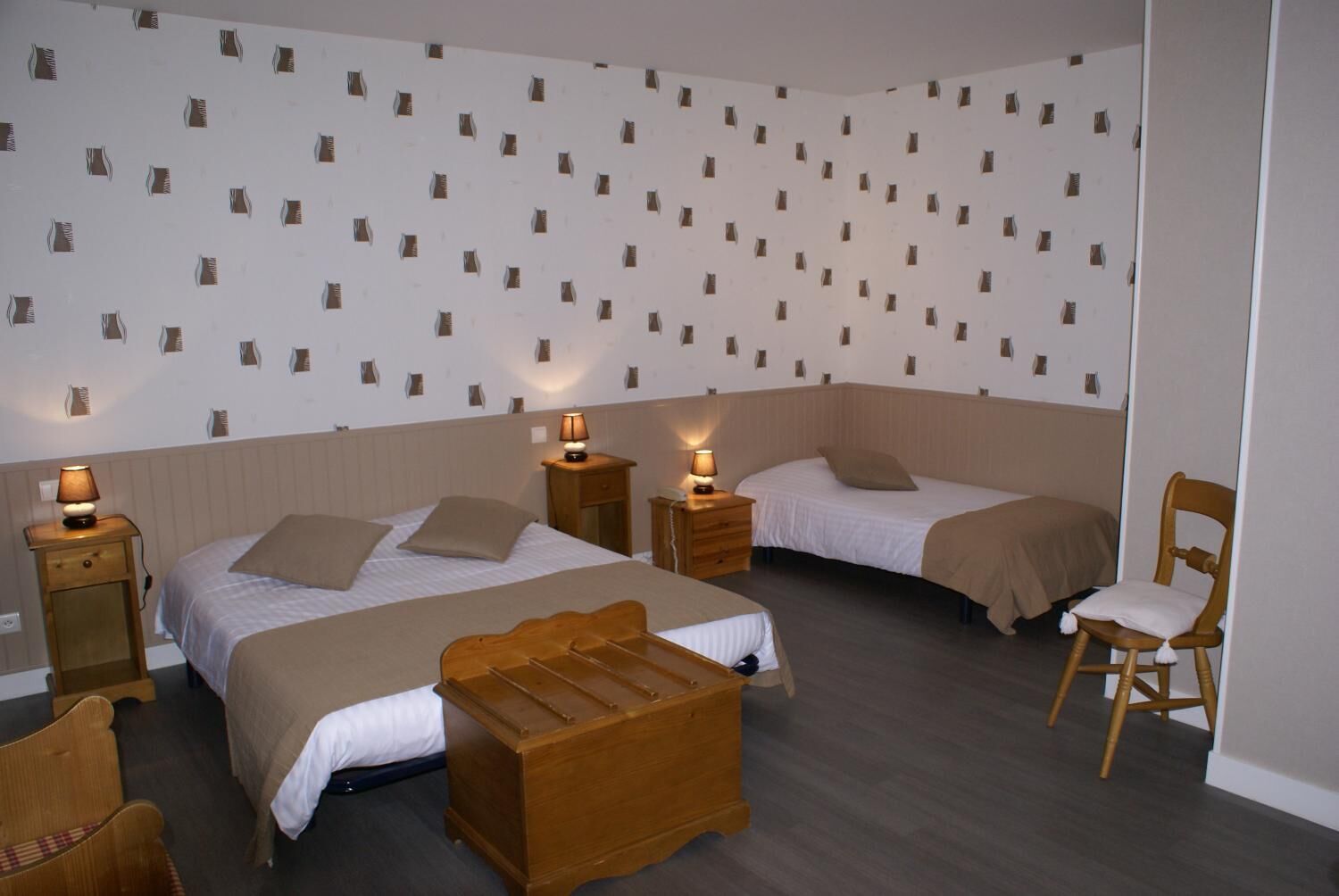 A hotel room with two beds, a wooden chest of drawers, a wooden chair, and a patterned wall.