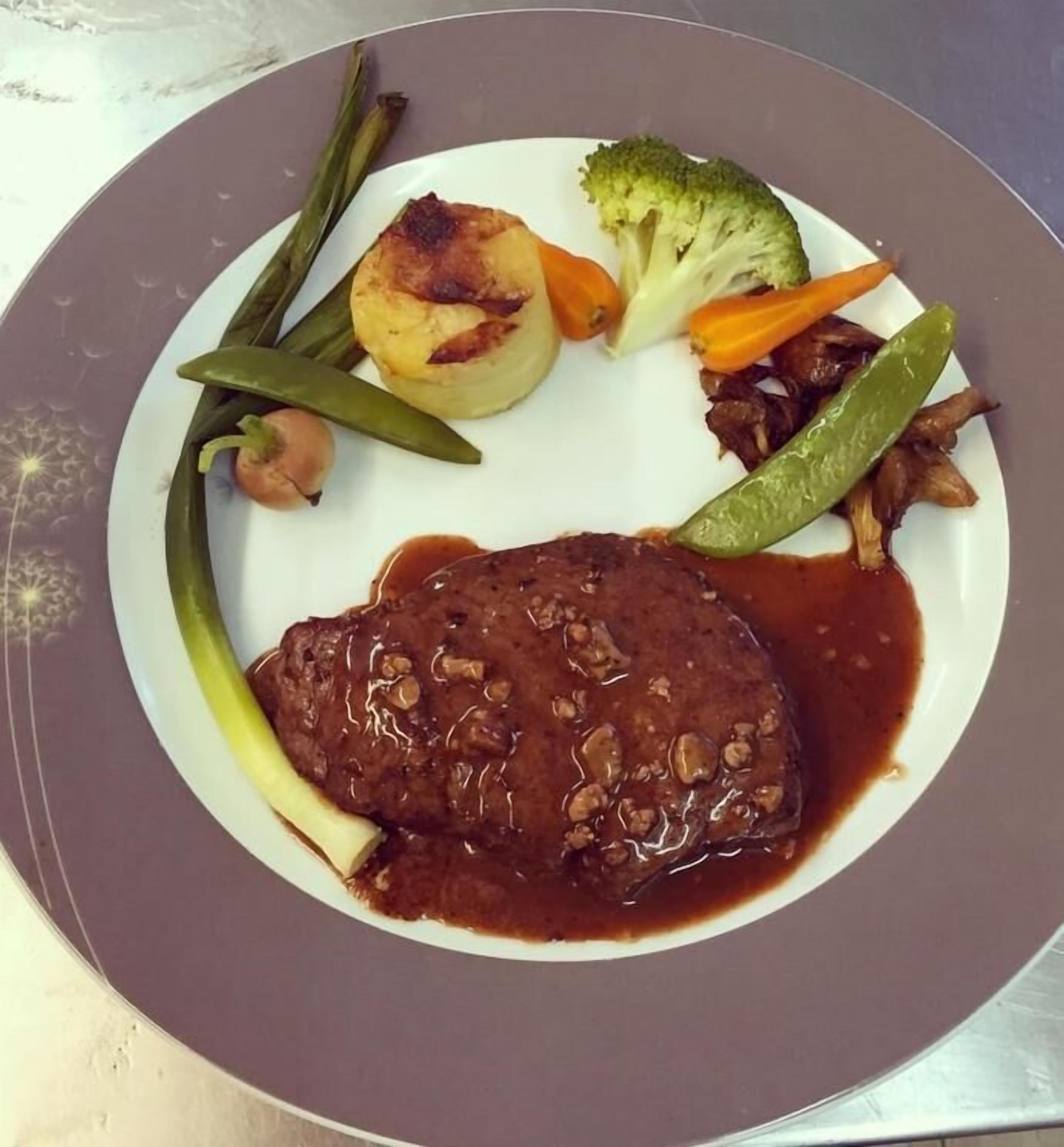 Een bord met een steak, groenten en saus.