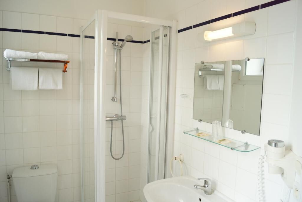 Un baño con cabina de ducha de vidrio, un lavabo, un espejo y un perchero para toallas.