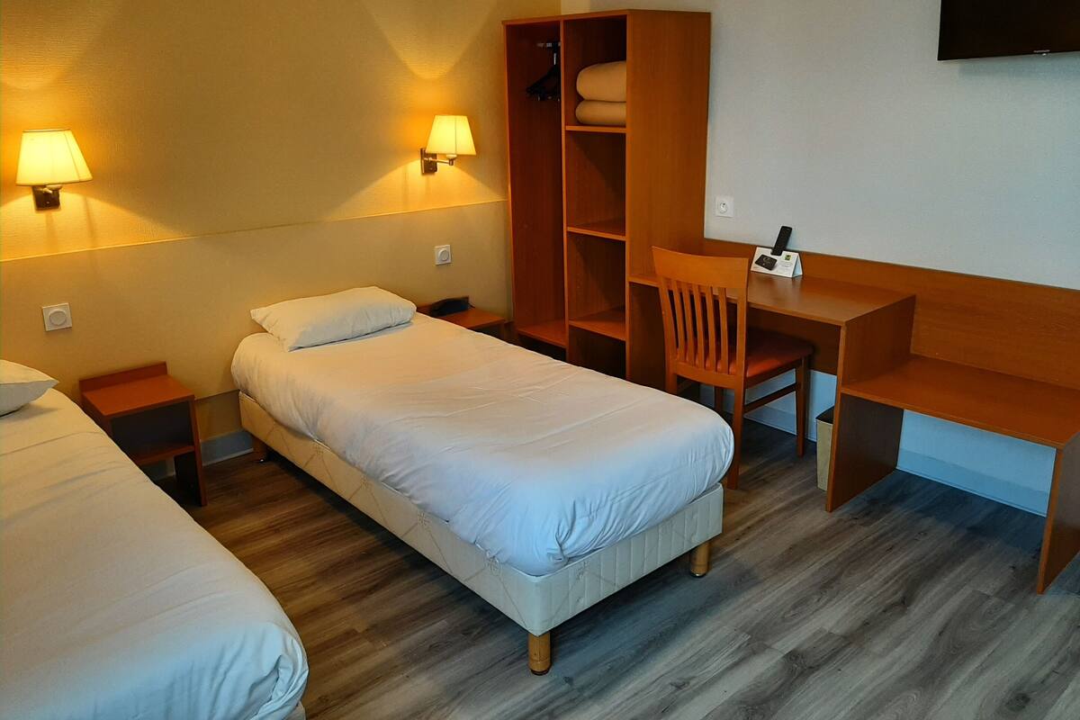 A hotel room with two single beds, a wooden desk, a chair, and a wardrobe.