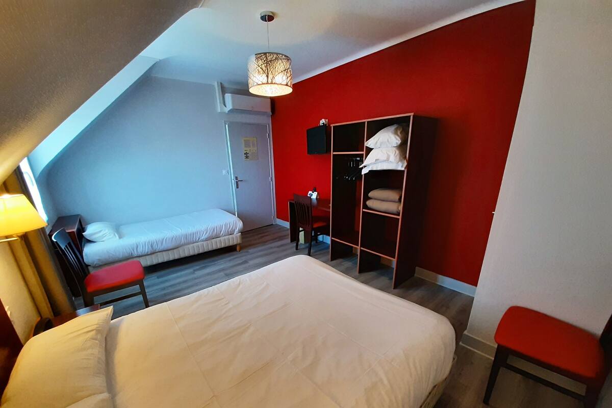 A bedroom with a large bed, a red wall, a wardrobe, and a small seating area.