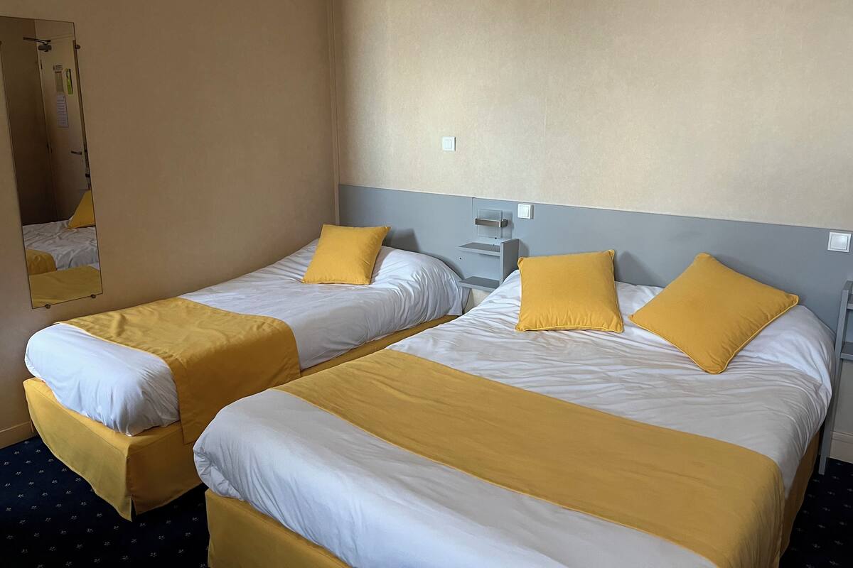 Une chambre d’hôtel avec deux lits, chacun agrémenté de draps blancs et jaunes, une table de chevet et un miroir.