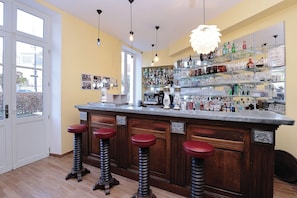 A bar area with a wooden counter, four stools, and a variety of bottles and glasses on shelves. - Relais Saint Louis (Belleme)
