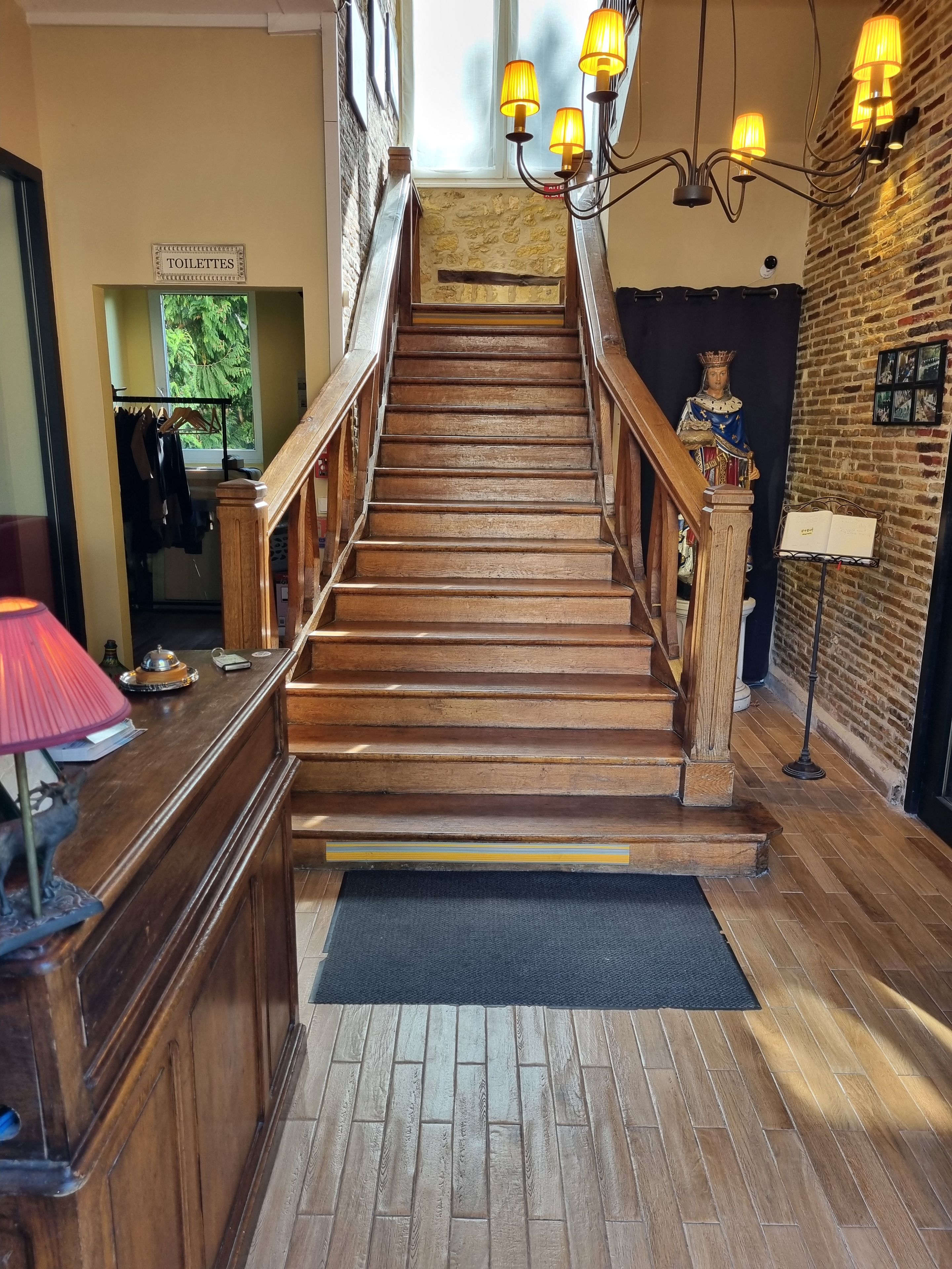 Un escalier en bois avec une rampe, un comptoir d’accueil et une statue sur le palier.