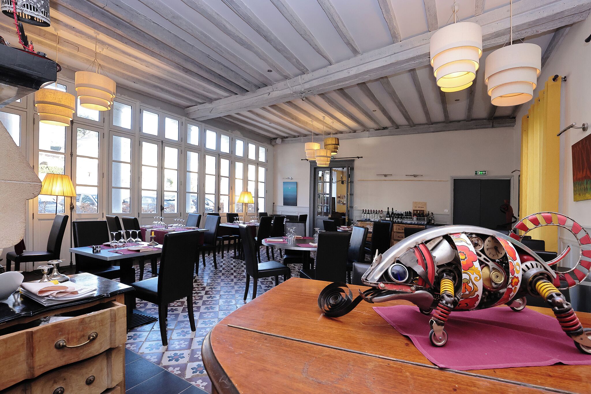 A restaurant with multiple dining tables, chairs, and hanging pendant lights.