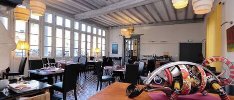 A restaurant with multiple dining tables, chairs, and hanging pendant lights.