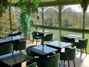 A conservatory with tables and chairs, large windows, and indoor plants.