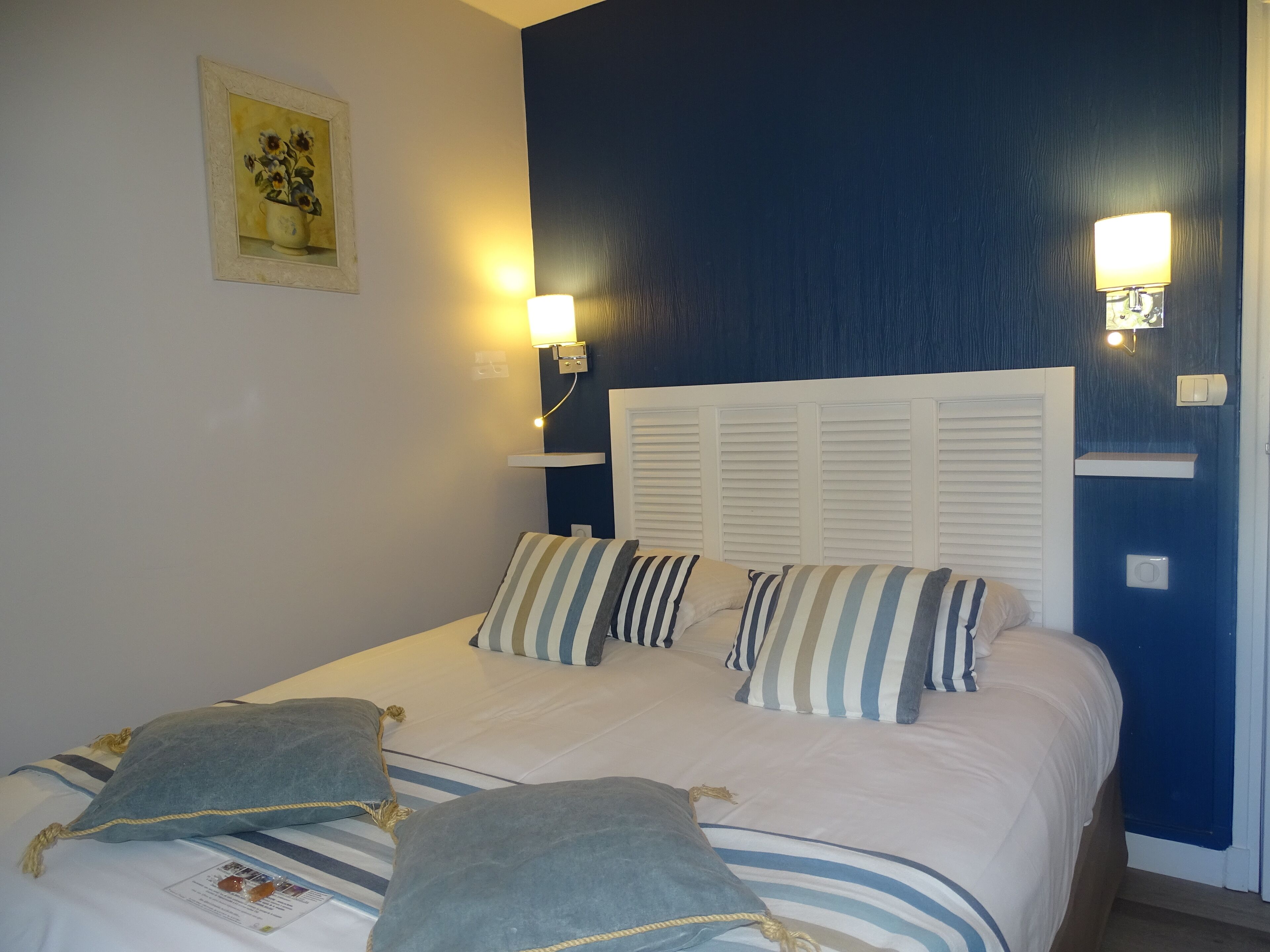 Een hotelkamer met een bed, gestreepte kussens, een nachtkastje en wandlampen.