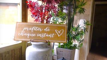 A wooden sign with text, a large vase, and potted plants in a room with tiled flooring.