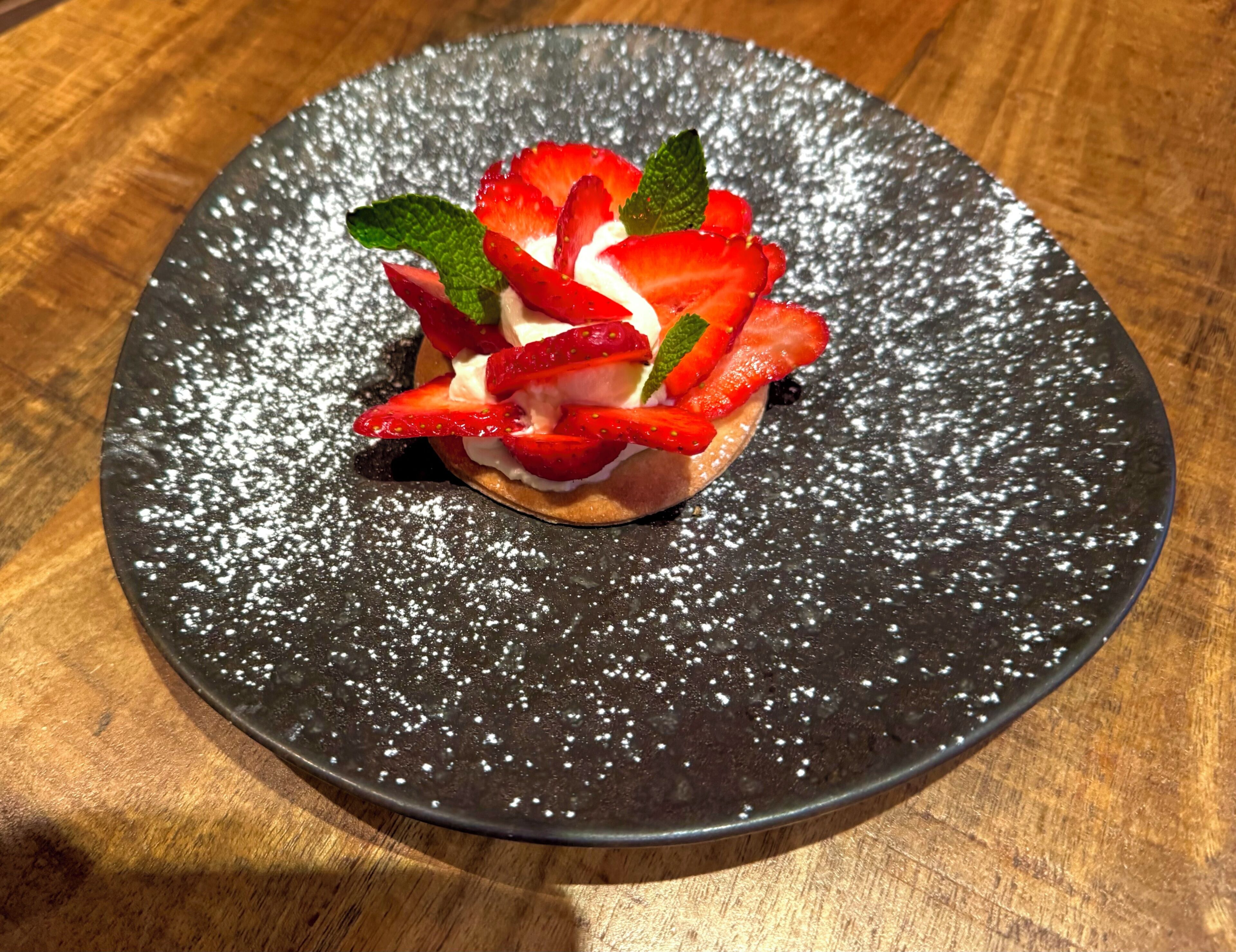 A dessert on a black plate with powdered sugar.