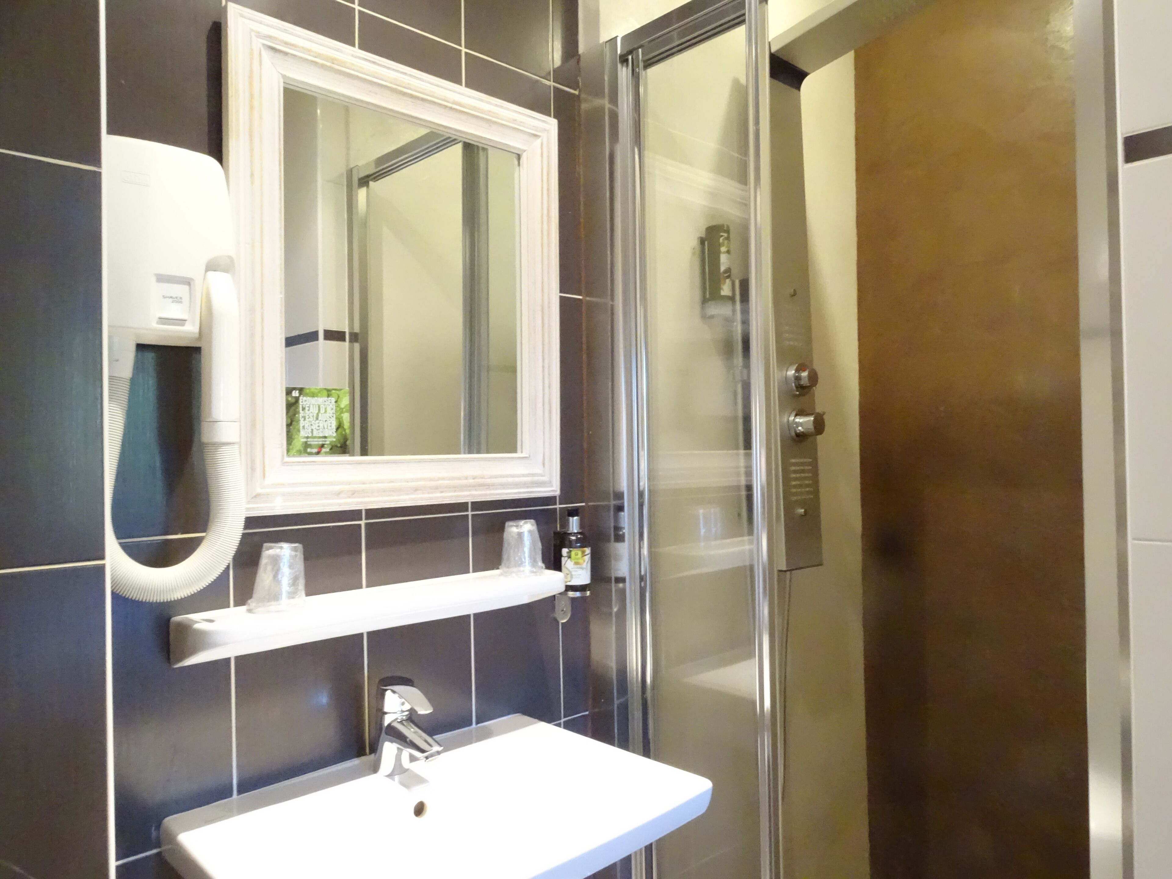 A bathroom with a white sink, a mirror, a towel dispenser, and a glass shower enclosure.