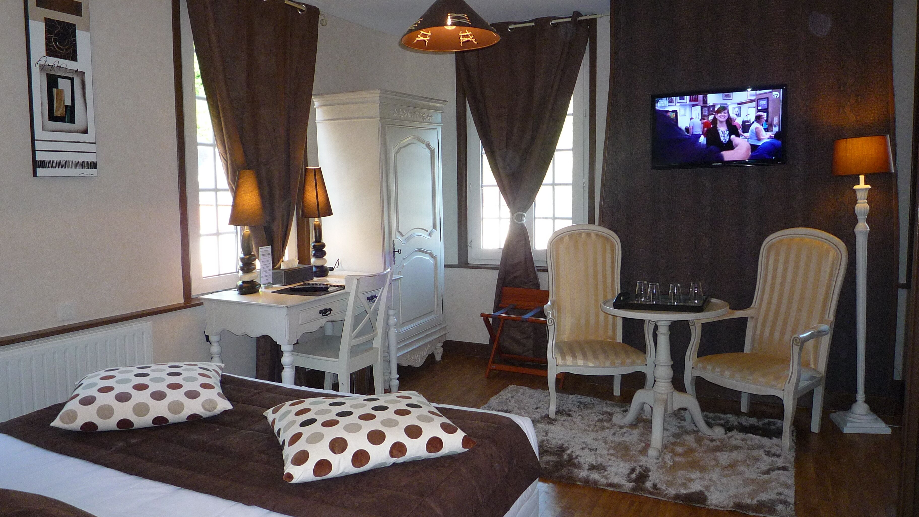 A hotel room with a bed, two chairs, a desk, a television, and a lamp.