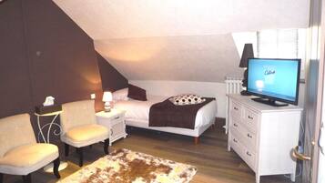 Ein Schlafzimmer mit einem Bett, einem Fernseher, einem Nachttisch, einem Sessel, einer Kommode und einem gemusterten Teppich.
