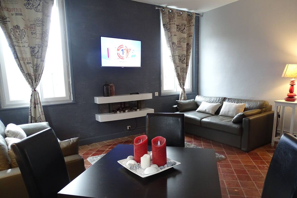 Una sala de estar moderna con una pared oscura, un sofá gris, un televisor montado sobre una estantería y una mesa con velas.