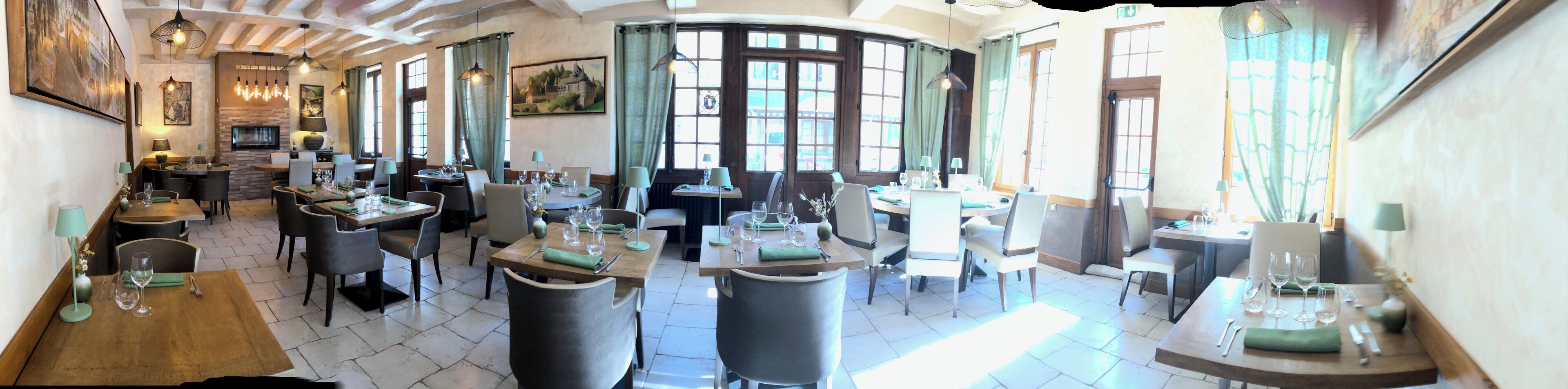 Een restaurant met verschillende eetgedeeltes, elk met tafels en stoelen. Er zijn grote ramen waardoor veel natuurlijk licht binnenkomt, en het interieur heeft zichtbare houten balken in het plafond.