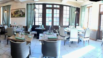 Een restaurant met verschillende eetgedeeltes, elk met tafels en stoelen. Er zijn grote ramen waardoor veel natuurlijk licht binnenkomt, en het interieur heeft zichtbare houten balken in het plafond.