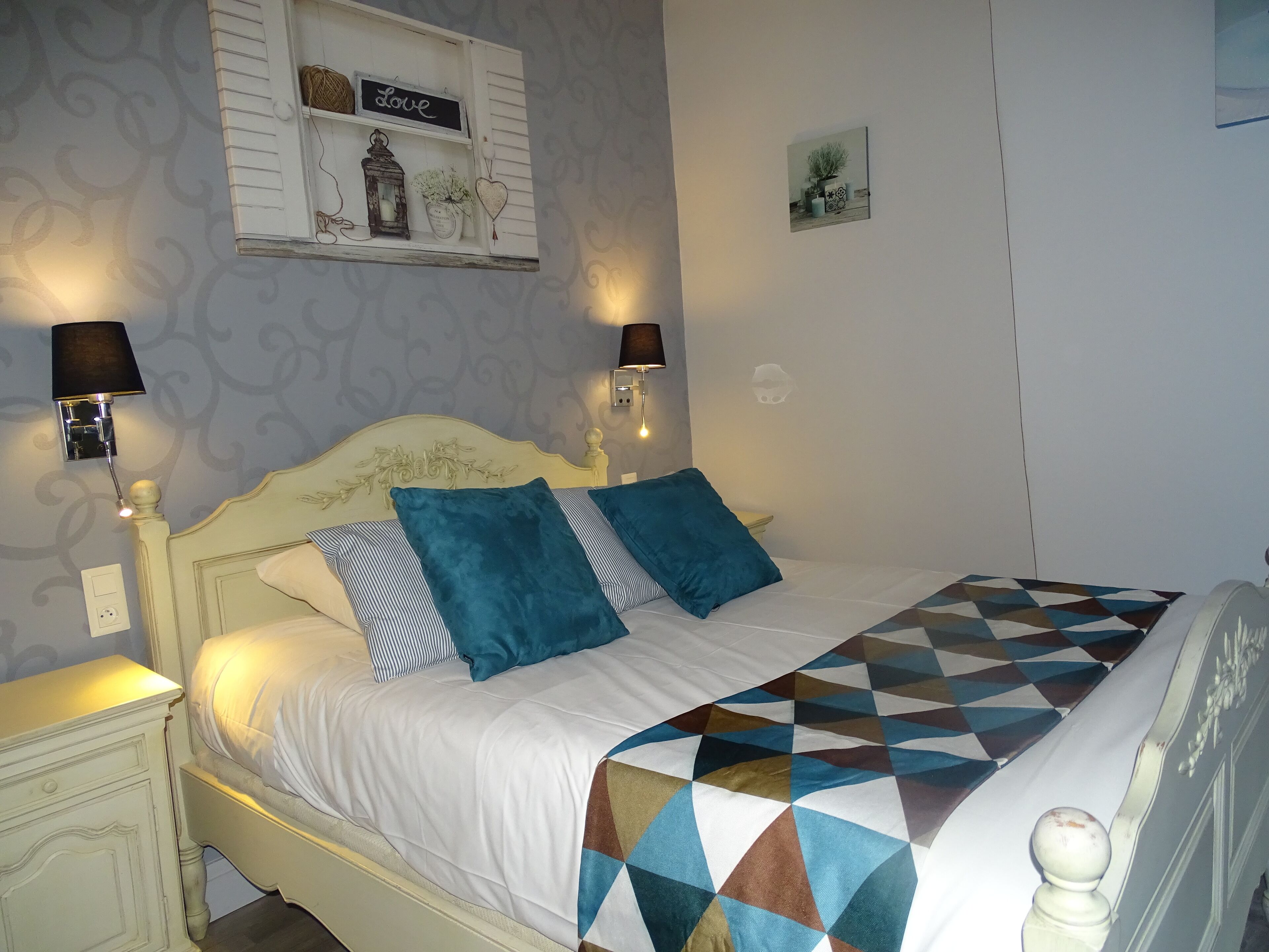 A neatly made bed with a geometric-patterned blanket, two pillows, and two wall-mounted lamps.