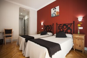 Two single beds with circular headboards, a red accent wall, and a wooden nightstand with a vase and lamp.