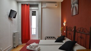 Habitación de hotel con dos camas, un televisor montado en la pared, un radiador y una cortina roja.